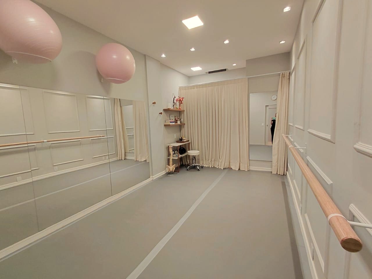 A sala de aulas da Salinha, com parede de espelhos, barra de ballet, bolas de pilates e cortinas claras