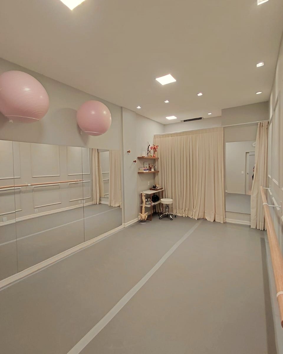 A sala da Salinha: espelhos, barra de ballet, bolas de pilates e cortinas claras